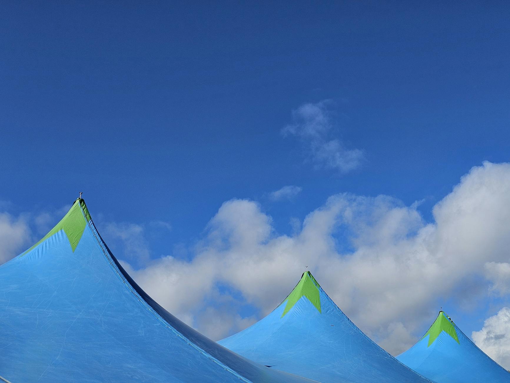 Vibrant blue tents with green tips against a clear sky with fluffy clouds.