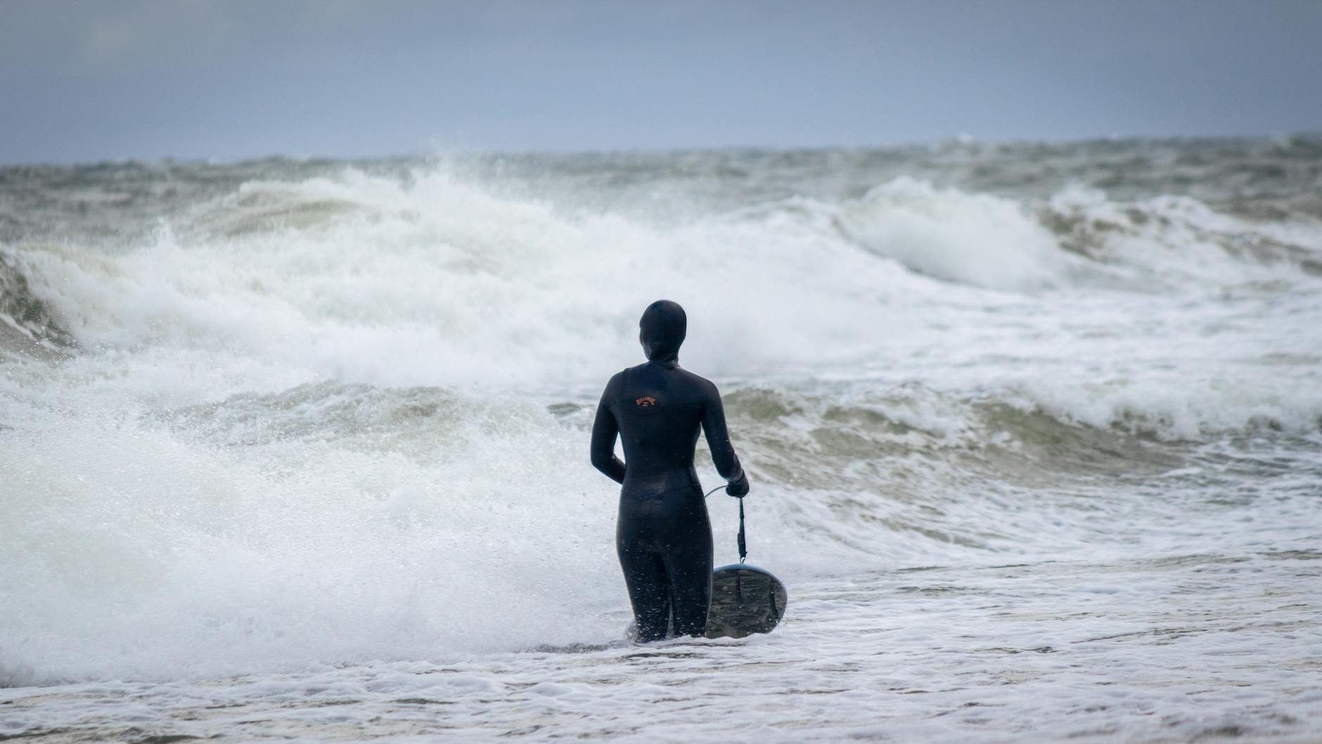 A woman in a wetsuit surfing in the rough Baltic Sea waves at Jastrzębia G&oacute;ra, Poland.