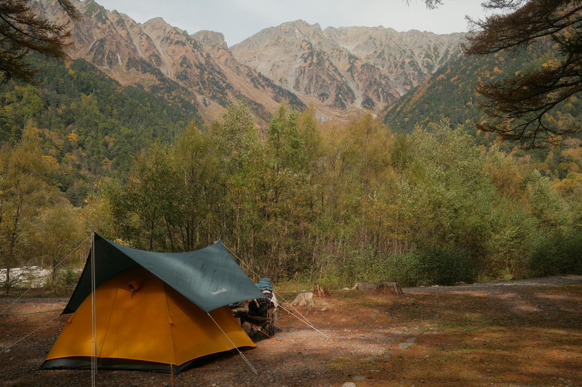 Serene autumn camping scene in Kamikochi, Matsumoto, with a vibrant tent and majestic mountain backdrop.