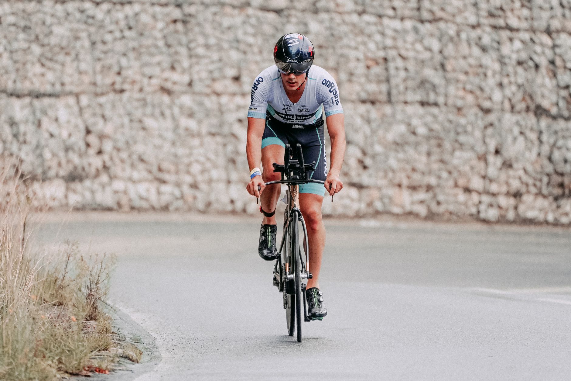 A male cyclist in full gear, riding on a road bike during an outdoor race.