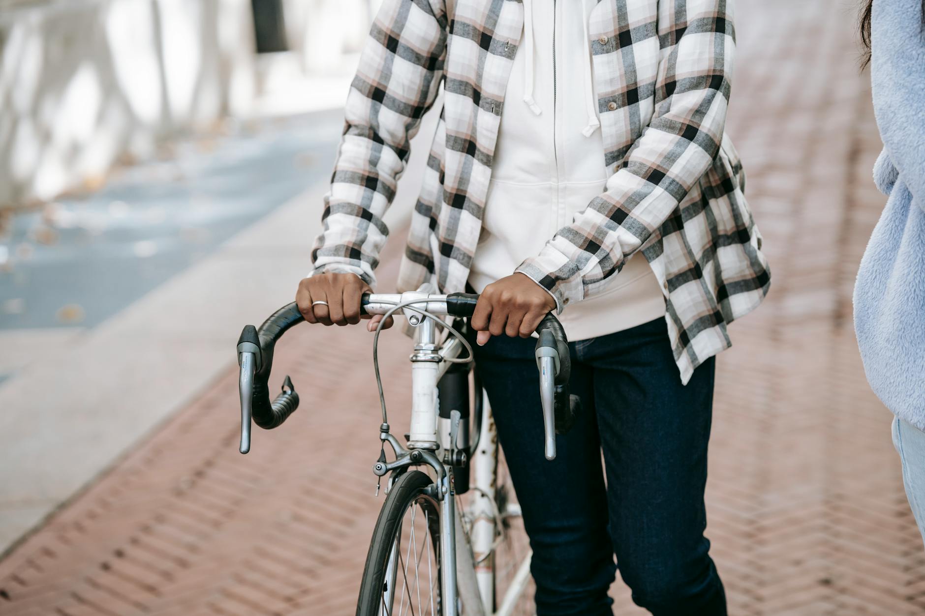 Crop faceless African American woman in casual outfit walking with bike near friend in park