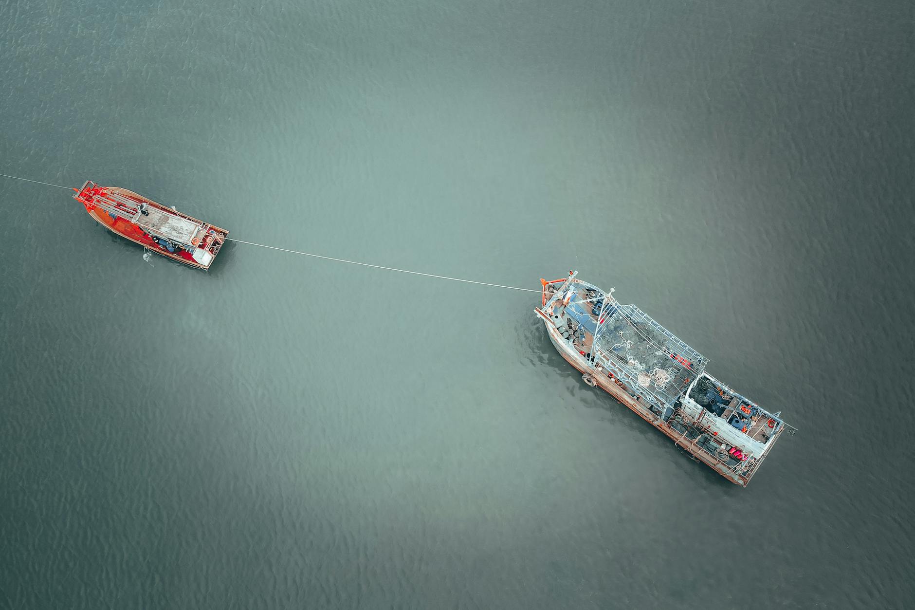 Drone view of barge with cargo and fishing tackle on rope with boat on river
